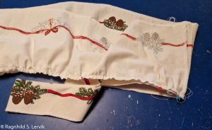 Kappen med girlander er rynket i ene kanten og i ferd med å festes på løpegangen med nåler.