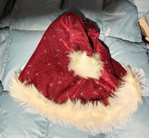 En nisselue i rød fløyel med hvit pelskant nederst og hvit pelsdusk. Det røde stoffet har stjerner i sølvglitter.